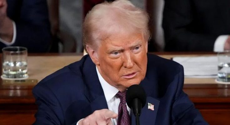 Donald Trump speaking into a microphone, wearing a dark blue suit, white shirt, and